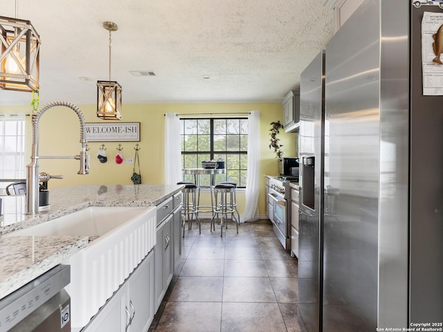 kitchen with hanging light fixtures, a sink, a textured ceiling, stainless steel appliances, and visible vents