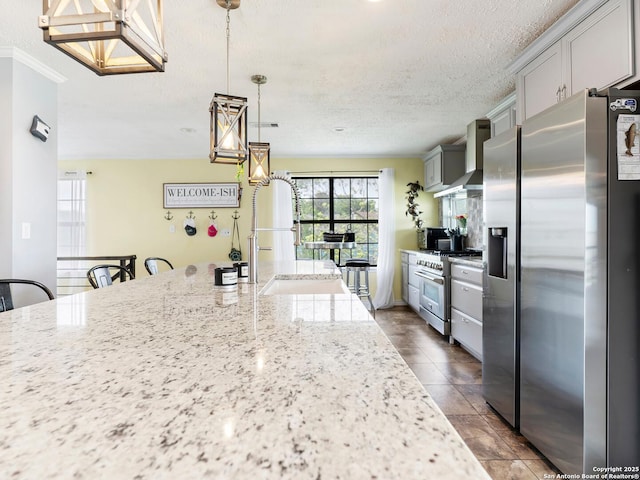 kitchen featuring a textured ceiling, a sink, light stone counters, stainless steel appliances, and wall chimney exhaust hood