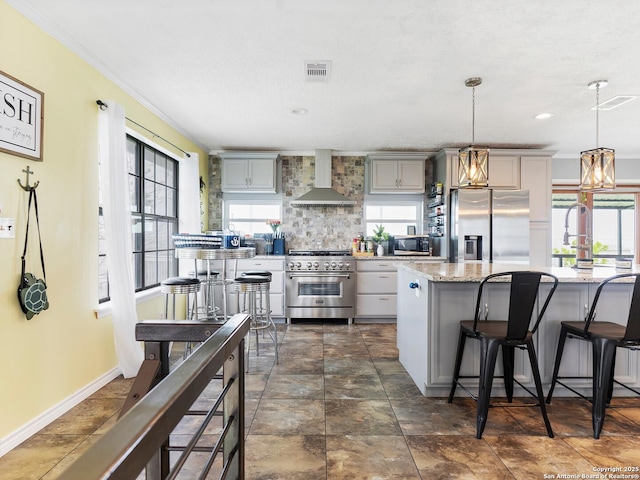 kitchen featuring wall chimney range hood, a kitchen breakfast bar, backsplash, visible vents, and stainless steel appliances