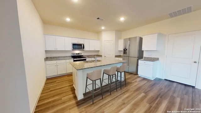 kitchen with a kitchen bar, visible vents, appliances with stainless steel finishes, wood finished floors, and white cabinets