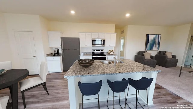 kitchen with white cabinets, appliances with stainless steel finishes, a sink, a kitchen island with sink, and a kitchen bar