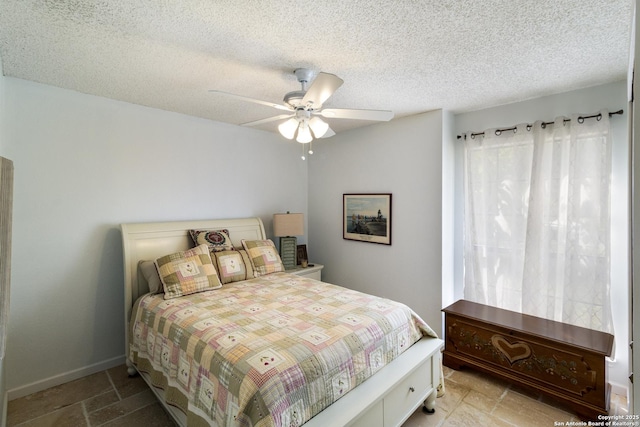 bedroom featuring a ceiling fan, baseboards, a textured ceiling, and stone tile flooring