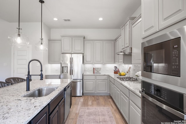 3818 Cualquiera, San Antonio, TX 78261 - kitchen with stainless steel appliances, a sink, light wood finished floors, decorative light fixtures, and under cabinet range hood