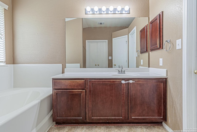 full bath featuring vanity, a textured wall, a garden tub, and visible vents