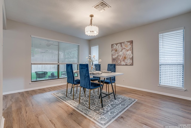dining room featuring visible vents, baseboards, wood finished floors, and a notable chandelier
