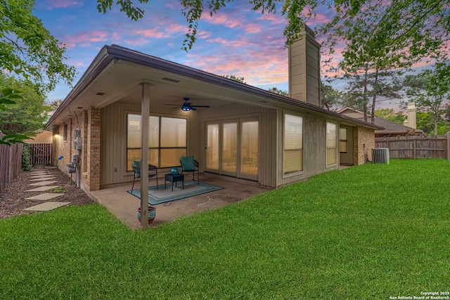 back of property at dusk with ceiling fan, a patio, a fenced backyard, a chimney, and a yard