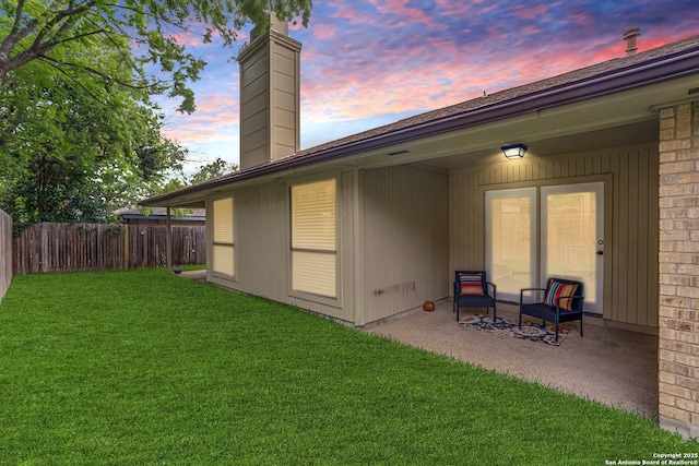 back of property at dusk featuring a patio, fence, a yard, and a chimney