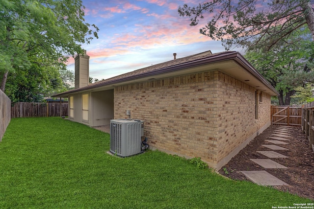 view of side of home with a lawn, brick siding, cooling unit, and a chimney