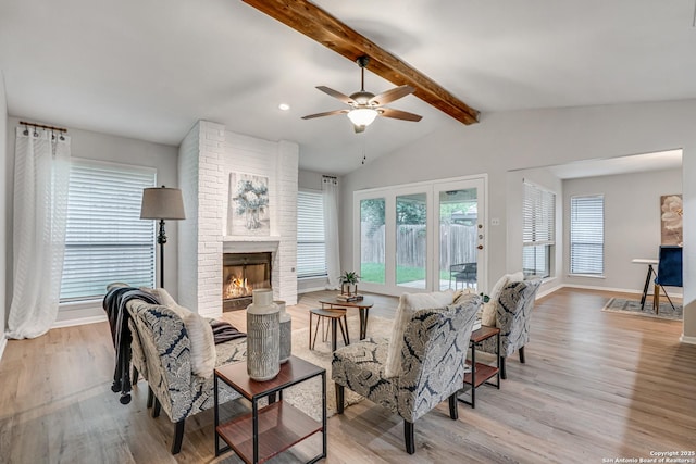 living room featuring a ceiling fan, a brick fireplace, wood finished floors, baseboards, and vaulted ceiling with beams
