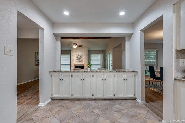 kitchen with a fireplace, baseboards, white cabinets, a ceiling fan, and a wealth of natural light
