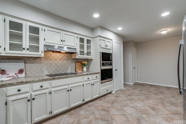 kitchen featuring light stone counters, stainless steel appliances, decorative backsplash, under cabinet range hood, and glass insert cabinets