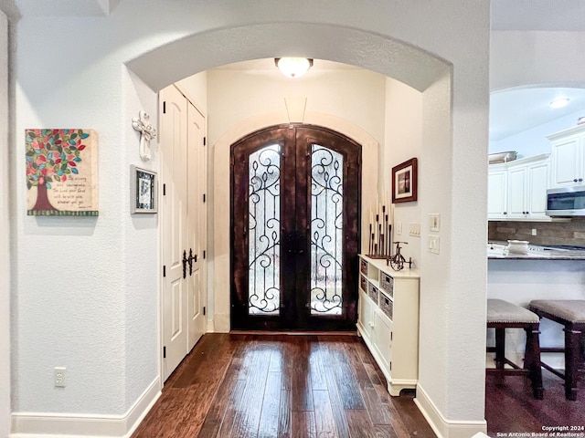 entryway featuring french doors, arched walkways, dark wood-style flooring, and a textured wall