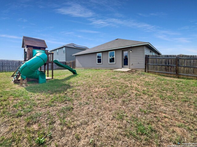 back of house with a fenced backyard, a playground, and a yard