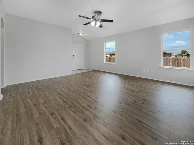 empty room featuring ceiling fan, arched walkways, vaulted ceiling, baseboards, and dark wood-type flooring