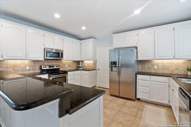 kitchen featuring decorative backsplash, appliances with stainless steel finishes, white cabinets, a peninsula, and dark stone countertops