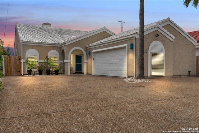 view of front of home with a tile roof, a garage, stucco siding, a chimney, and driveway