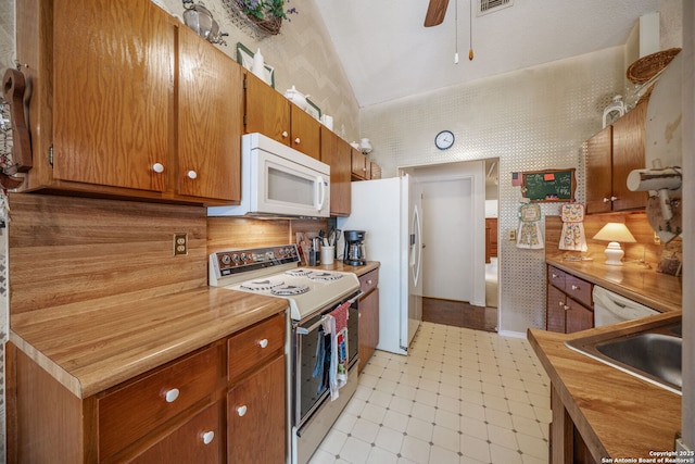 kitchen with decorative backsplash, brown cabinets, a sink, wallpapered walls, and white appliances