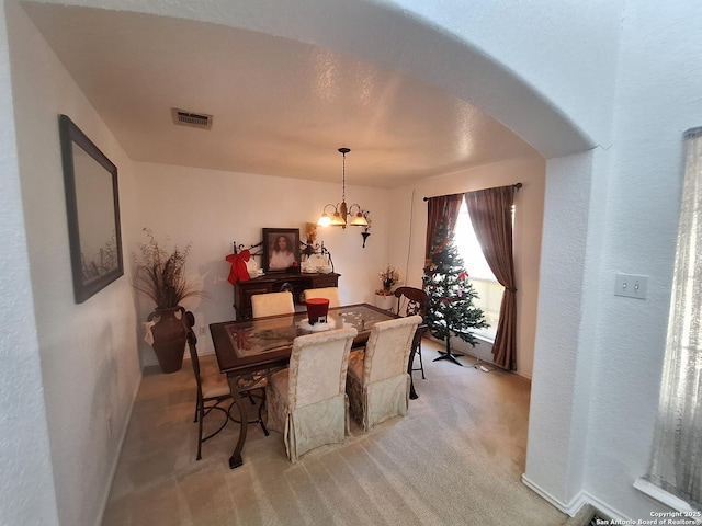 dining space featuring light colored carpet, baseboards, visible vents, and an inviting chandelier