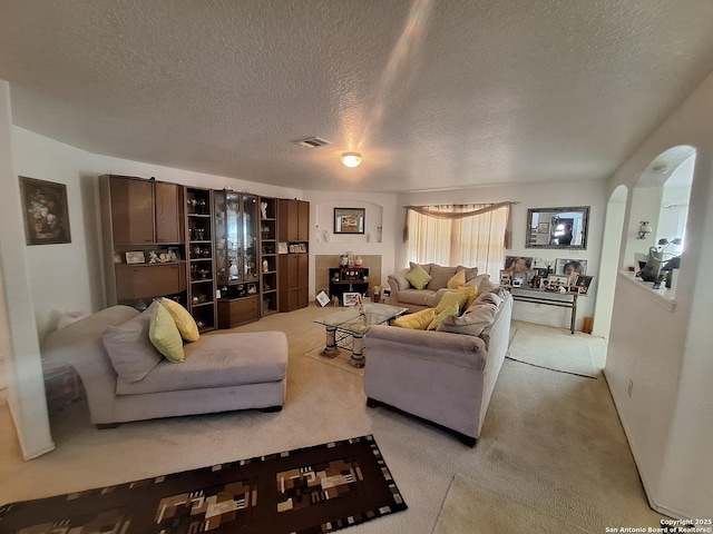 living area with arched walkways, carpet, a textured ceiling, and visible vents