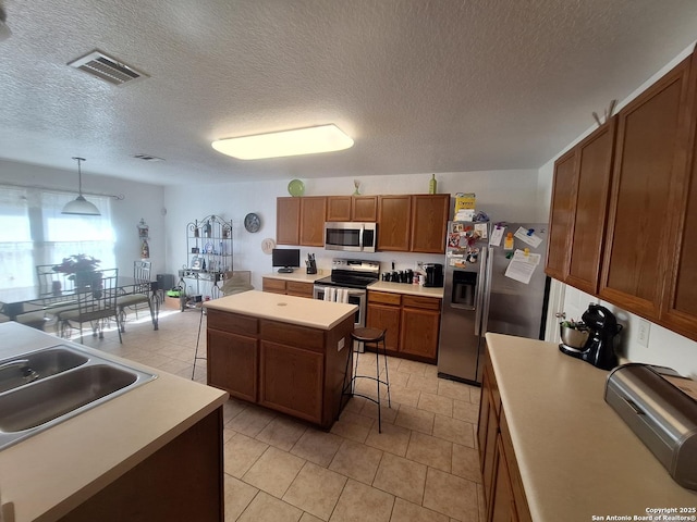kitchen with a kitchen island, visible vents, appliances with stainless steel finishes, a sink, and light countertops