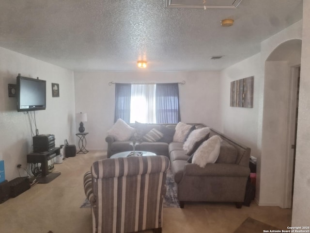 carpeted living area with arched walkways, attic access, and a textured ceiling