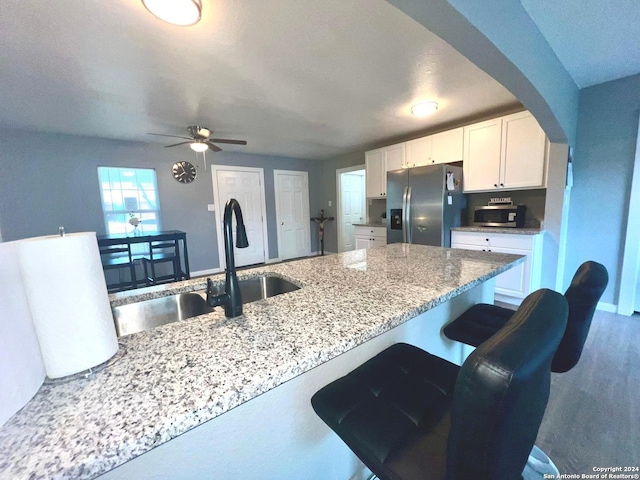 kitchen with light stone countertops, arched walkways, white cabinets, stainless steel fridge with ice dispenser, and a sink