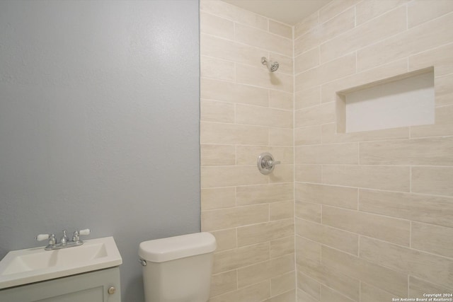 bathroom featuring toilet, a tile shower, and vanity