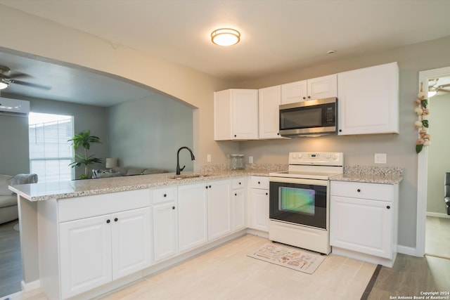 kitchen with a peninsula, white range with electric cooktop, stainless steel microwave, a wall unit AC, and a sink