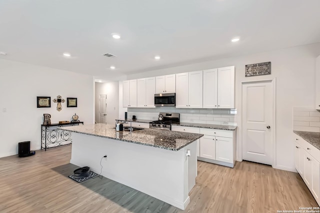 kitchen with appliances with stainless steel finishes, tasteful backsplash, a sink, dark stone counters, and light wood-style flooring