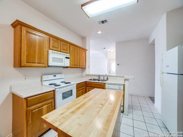 kitchen featuring a peninsula, light tile patterned floors, a sink, visible vents, and white appliances