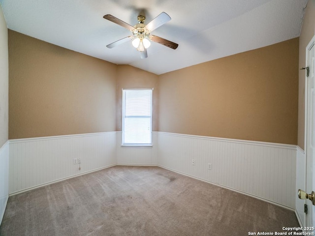 unfurnished room featuring carpet flooring, a ceiling fan, vaulted ceiling, and wainscoting