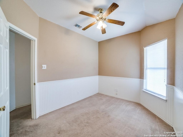 carpeted spare room with a ceiling fan, a wainscoted wall, and visible vents