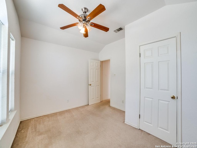unfurnished bedroom featuring lofted ceiling, ceiling fan, visible vents, and light colored carpet