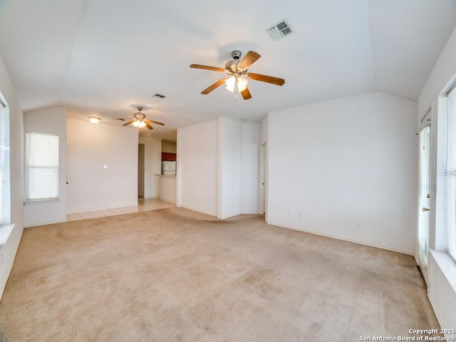unfurnished living room with vaulted ceiling, light colored carpet, a ceiling fan, and visible vents