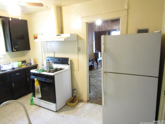 217 Lancaster, San Antonio, TX 78214 - kitchen with wall chimney range hood, white appliances, dark cabinets, a ceiling fan, and light tile patterned floors