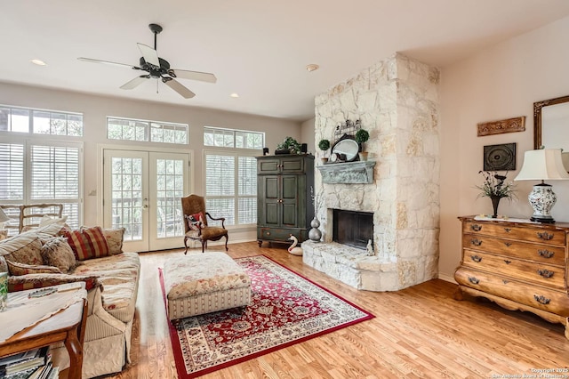 living room featuring french doors, ceiling fan, a stone fireplace, and wood finished floors