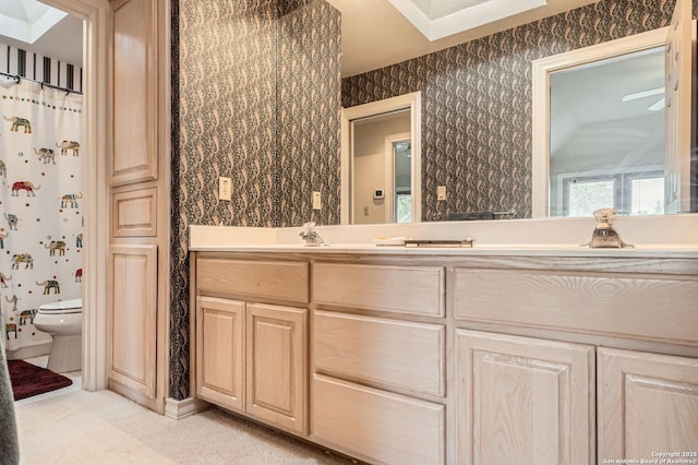 bathroom featuring double vanity, a sink, toilet, and wallpapered walls