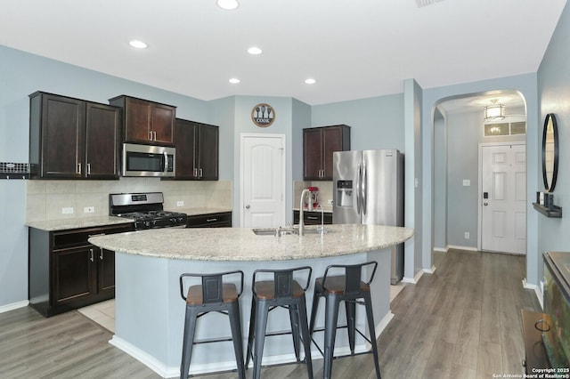 kitchen featuring dark brown cabinetry, a sink, arched walkways, stainless steel appliances, and a kitchen bar