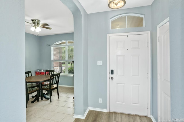 foyer entrance featuring arched walkways, a ceiling fan, light tile patterned flooring, and baseboards