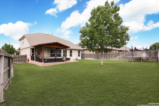 rear view of property featuring ceiling fan, a trampoline, a lawn, a fenced backyard, and a shingled roof