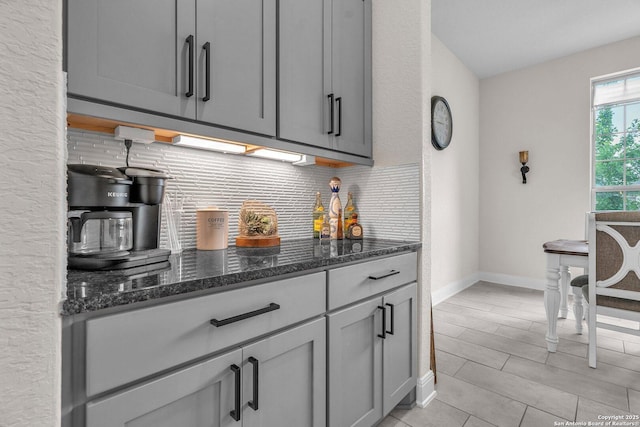 kitchen with dark stone counters, baseboards, gray cabinetry, and decorative backsplash