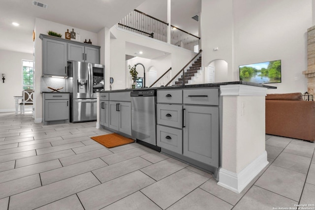 kitchen with dark countertops, a high ceiling, stainless steel appliances, open floor plan, and gray cabinetry
