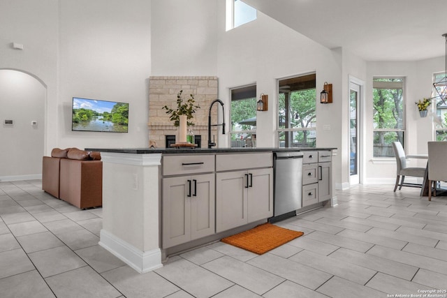 kitchen with a high ceiling, a sink, arched walkways, light tile patterned floors, and stainless steel dishwasher