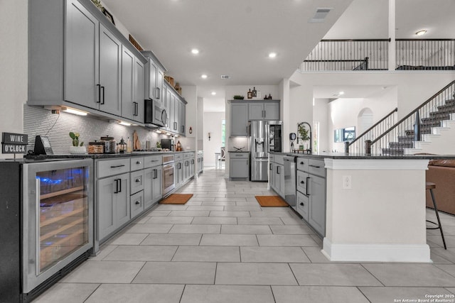 kitchen with decorative backsplash, dark countertops, gray cabinetry, wine cooler, and stainless steel appliances