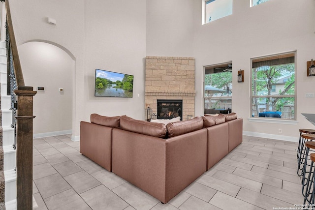 living area with arched walkways, a fireplace, light tile patterned floors, baseboards, and a high ceiling