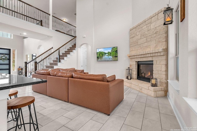 living area featuring arched walkways, a stone fireplace, light tile patterned floors, a towering ceiling, and stairway