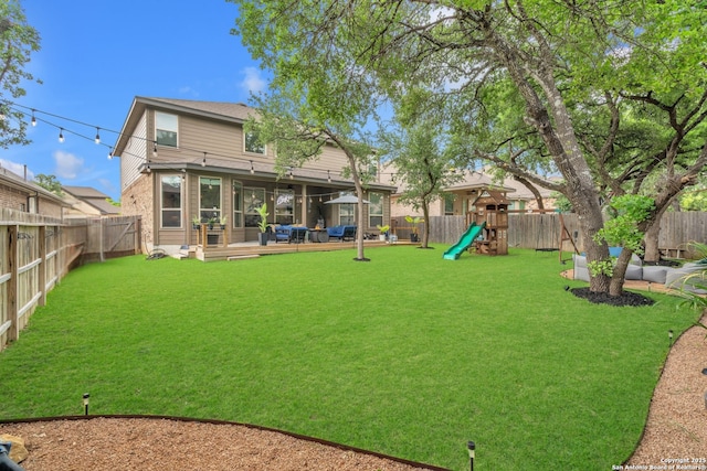 rear view of property with a playground, a lawn, and a fenced backyard