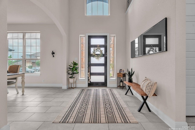 entryway featuring arched walkways, baseboards, light tile patterned flooring, and a high ceiling