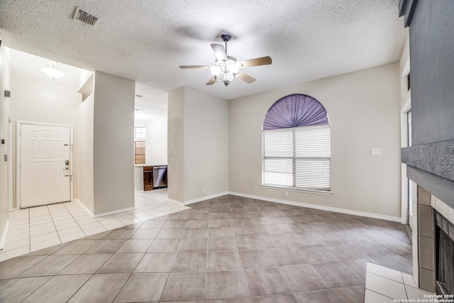 10210 Apricot Fld, San Antonio, TX 78245 - unfurnished living room featuring visible vents, a textured ceiling, a tiled fireplace, a ceiling fan, and light tile patterned floors