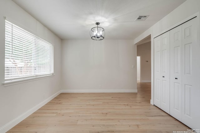 unfurnished dining area with baseboards, light wood-style flooring, a notable chandelier, and visible vents